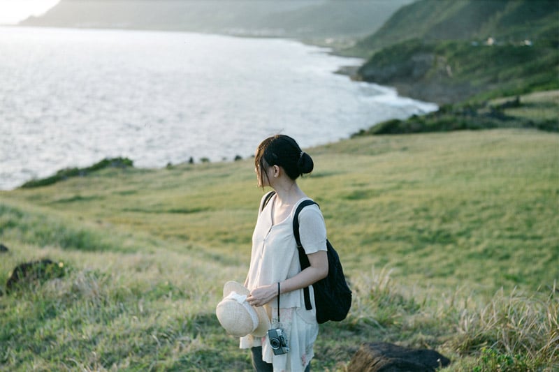 Girl standing on a field, looking at the sea